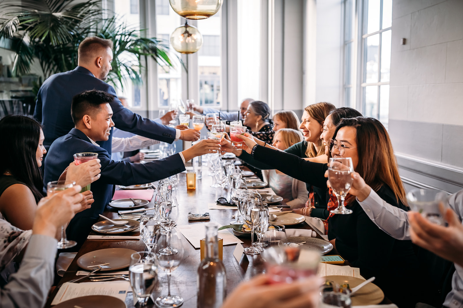 An inclusive and intimate wedding and elopement photographer, Xilo Photography, Kati Douglas who is based in Oakland, California in the bay area, took this picture of a same sex gay couple on their wedding elopement day as the two grooms toast at the restaurant with their family and loved ones as they celebrate their wedding day in their tuxes in CA after leaving their intimate wedding venue. Ever wondered what is an intimate wedding or what would be considered a small wedding? This is a great example of both! 